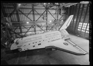 Photo of port side view of the Orbiter Discovery at the Vehicle Assembly Building at NASA's Kennedy Space Center. Orbiter Discovery is parked on the ground. The Orbiter Discovery is pointed to the left, framed by a warehouse.r