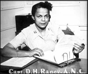 Black and white photograph of Della Raney in a captain’s uniform, sitting at a desk, flipping through paper charts. 