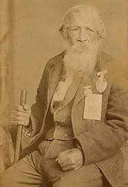 Sepia tone photograph of an elderly Jordan Noble sitting down and wearing multiple medals on his breast pocket