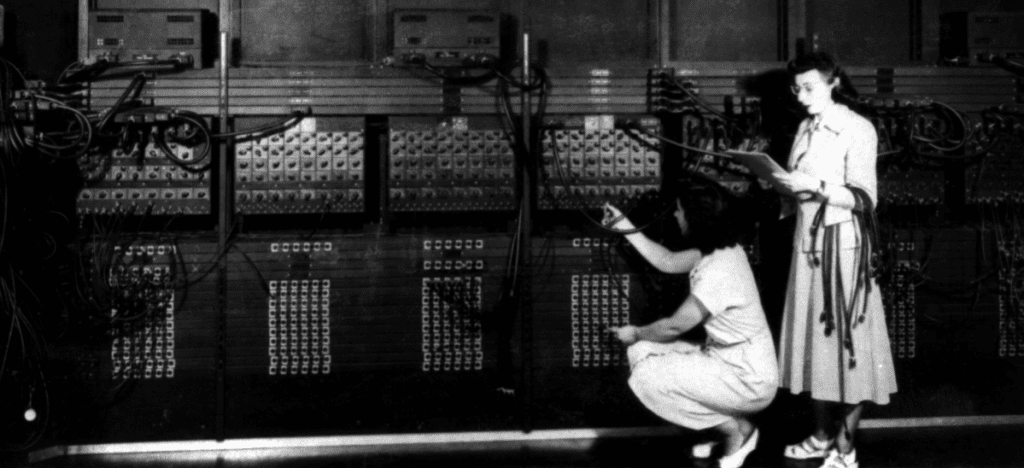 Two women rewire a computer that takes up an entire wall