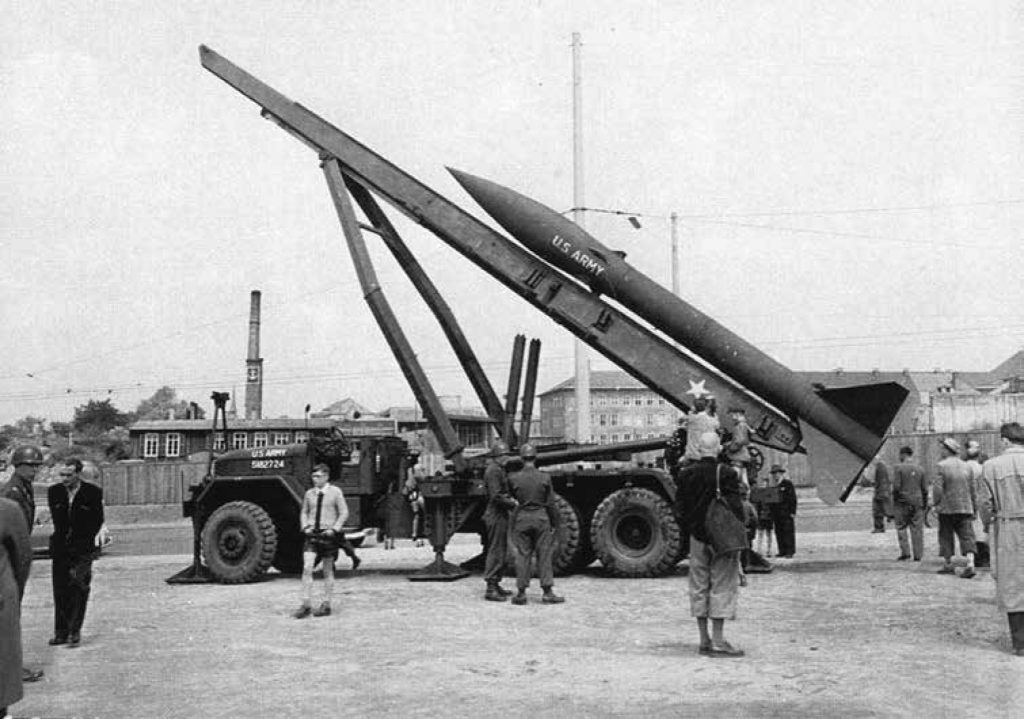 Large nuclear rocket on the back of a vehicle surrounded by Soldiers and German citizens