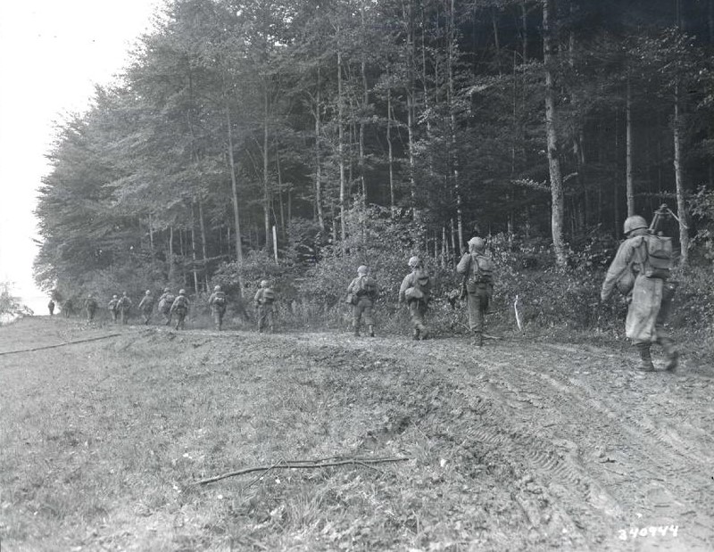 Soldiers walking down a muddy road next to a forest