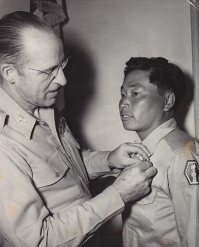 A man pins a medal on the uniform of a Japanese American soldier