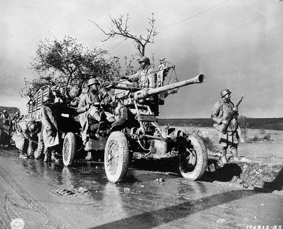 Group of Black Soldiers with artillery and automobiles stopped on the side of a road