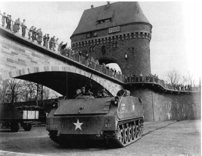 US Army tank driving past a bridge full of onlookers