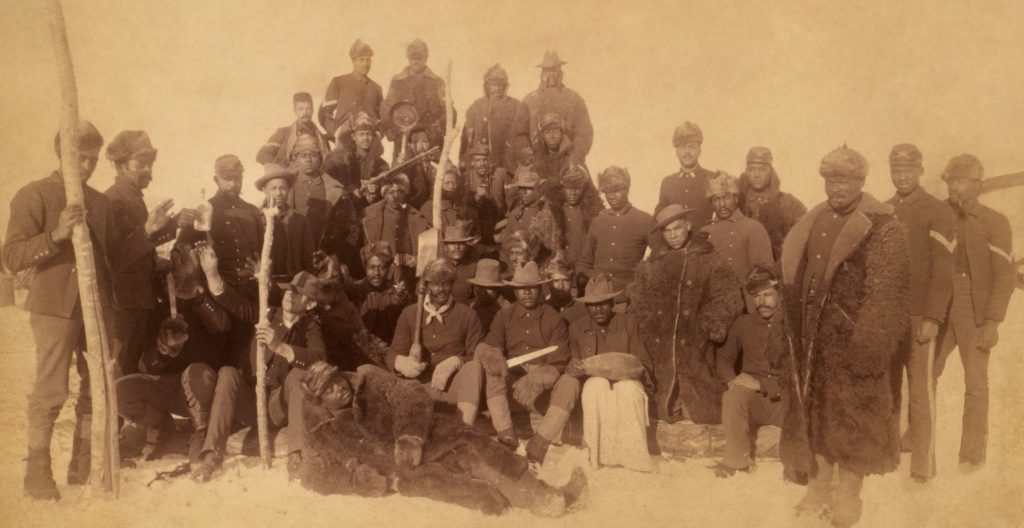 Group of mostly Black soldiers posed in late 19th century era uniforms