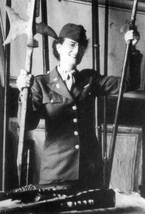 Edith Standen in uniform holding museum artifacts including an old axe.
