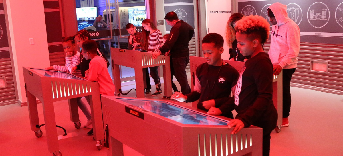 Groups of children stand at touch screen kiosks