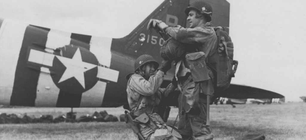 Two Soldiers in front of an airplane. One Soldier inspects the gear of the other soldier.