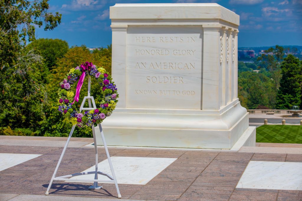 Wreath with Purple and yellow flowers and purple ribbon sitting in front of the Tomb of the Unknown Soldier.