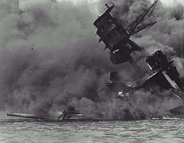 A battleship lists to one side surrounded by a plume of thick smoke.