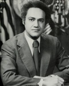 Clifford Alexander wearing a suit posing in front of an American flag