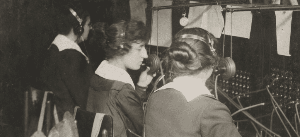 Three women wearing headphones sit at a switchboard 