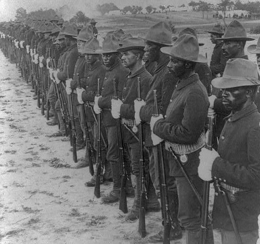 Line of Black Soldiers in formation wearing brimmed hats with a dome pinched into 4 quadrants at the top 