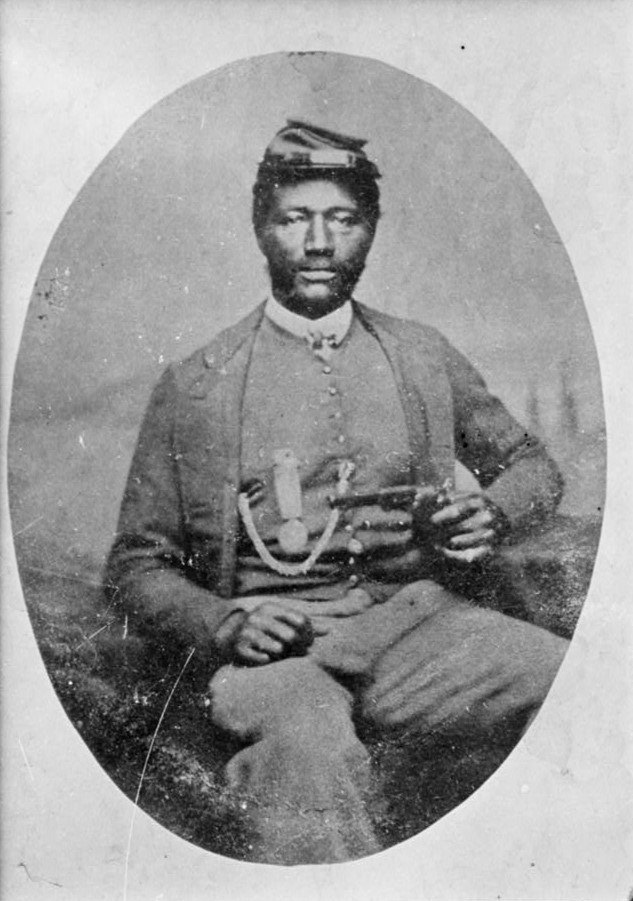 Black Soldier seated holding a hand gun and wearing a medal