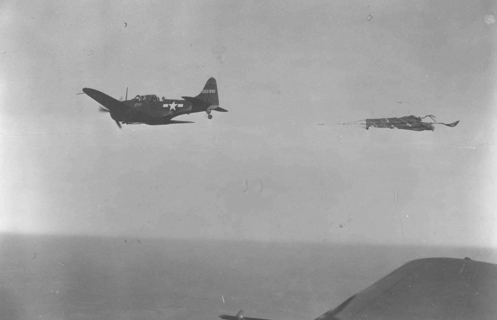 Single engine propeller plane flies through the air towing a tattered cloth sleeve
