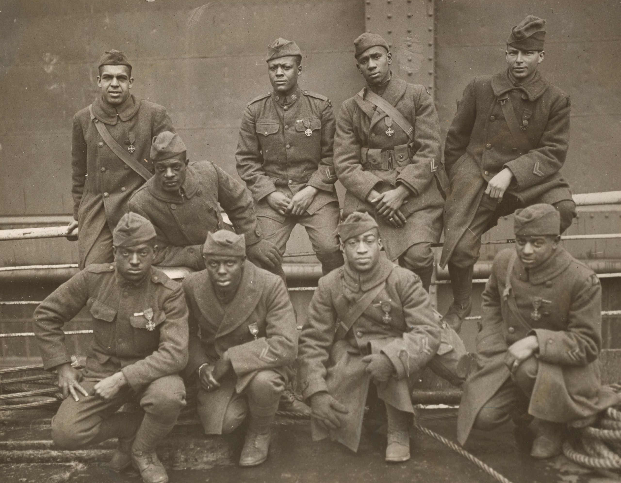 9 Black American Soldiers pose on in uniform. All have the Croix de Guerre medal pinned to their left breast pocket.