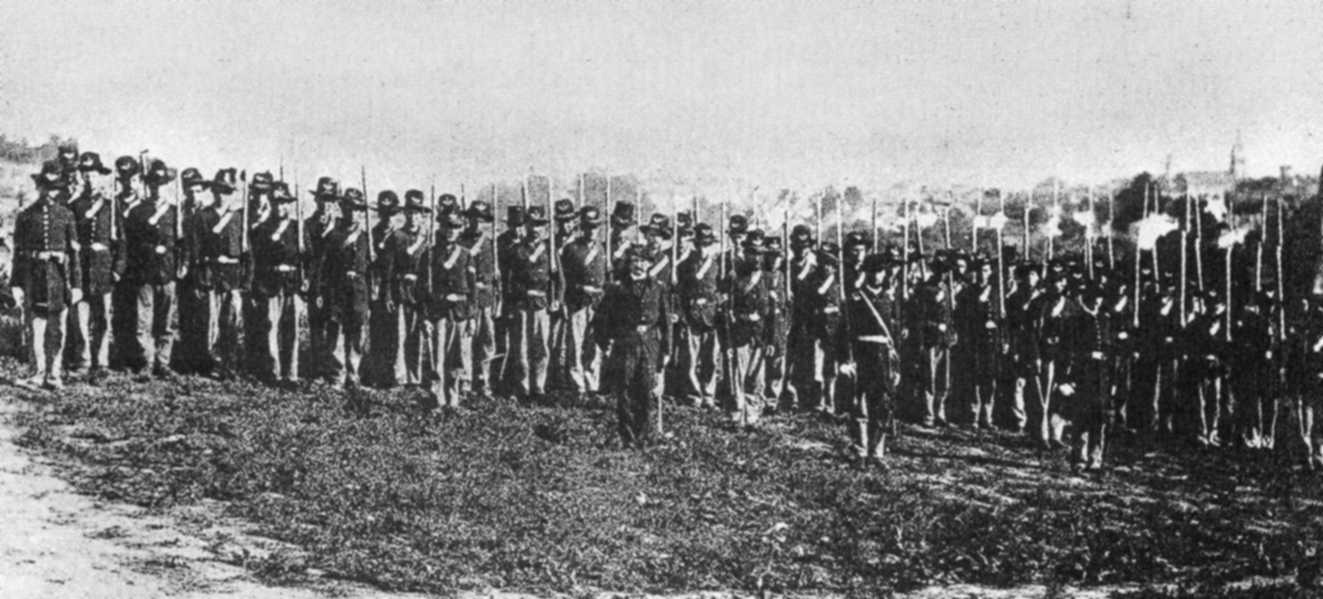 A group of Soldiers in uniform pose with rifles at their sides. 