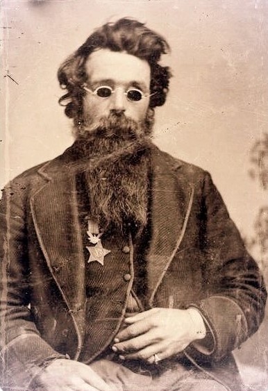 A man in a coat, seated, wearing sunglasses with a Medal of Honor pinned on his right breast.