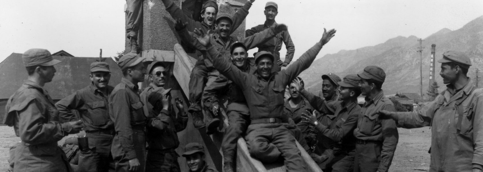 A group of Soldiers surround and sit on a playground slide. Their hands are upraised in celebration. 