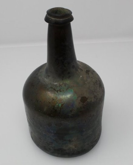 Dark green/brown glass bottle with some iridescence or patination on the surface. Object ID 2019.5.19. Courtesy of The Fort Ticonderoga Museum Collection.