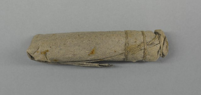Paper cartridge consisting of folded over tube of gray laid paper containing black powder, lead ball and buckshot all secured with a linen string. Object ID 2013.0326. Courtesy of The Fort Ticonderoga Museum Collection.