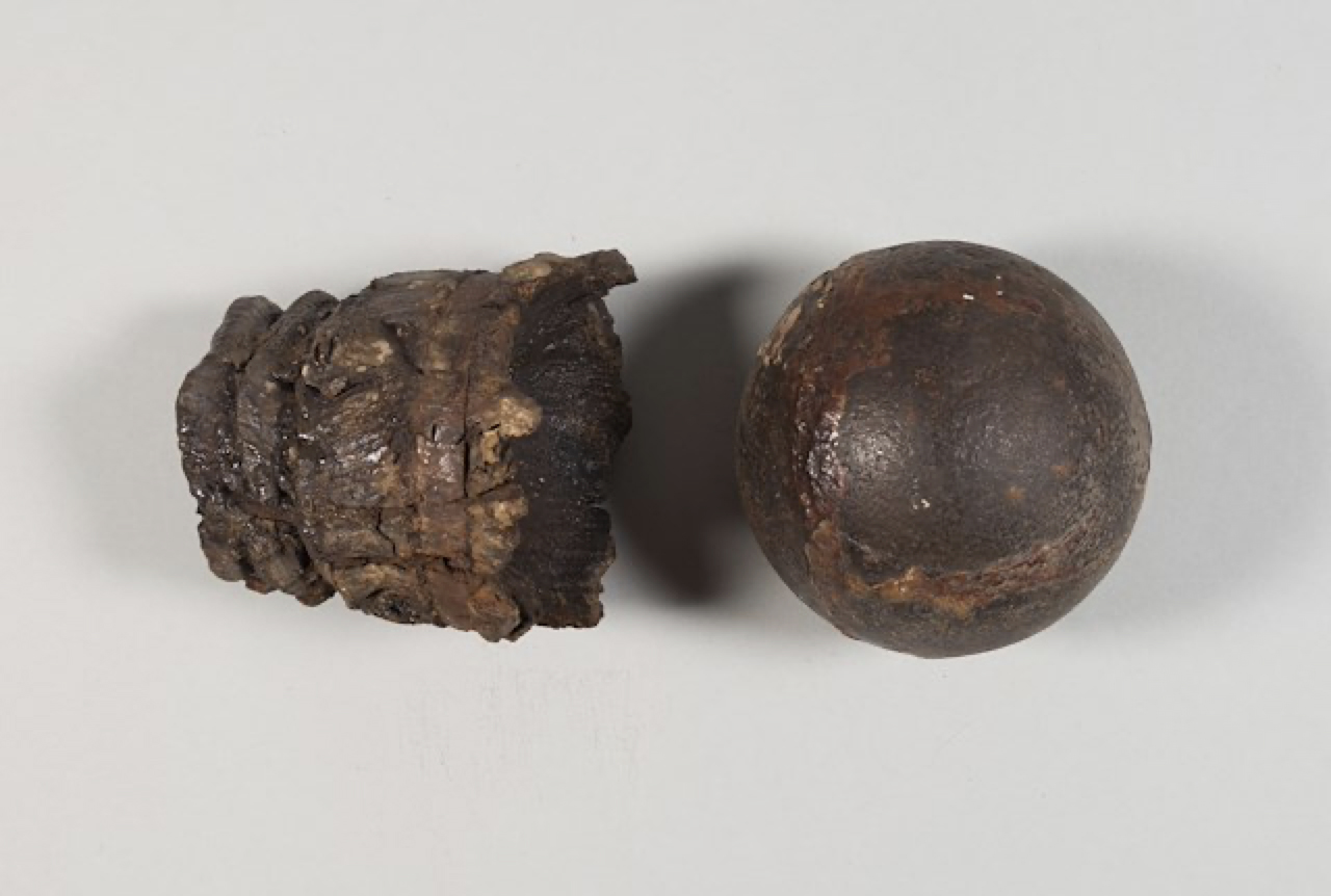 Strapped shot or fixed shot, ca. 1776-1781. This ammunition was designed for a British 3-pounder cannon. The cannonball would have been attached to the wooden base. The wooden base would also have had a bag of gunpowder tied to it. The grooves in the wooden base show where the straps holding the cannonball and the bag of gunpowder would have been. Object ID 2024.7.7a-b. Courtesy of the Fort Ticonderoga Museum Collection.