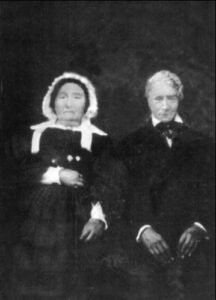 A 19th-century portrait painting depicting an elderly couple in formal attire; the woman is in a dark dress and white bonnet, and the man is in a dark suit.