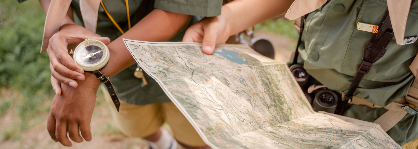 Two scouts study a topographic map outdoors while one holds a compass.